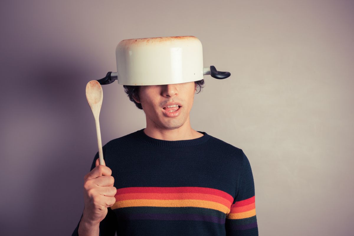 Man wearing a cooking pot as a helmet and holding a wooden spoon symbolizing reckless speculation and the risks of investing in meme coins and questionable altcoin projects.