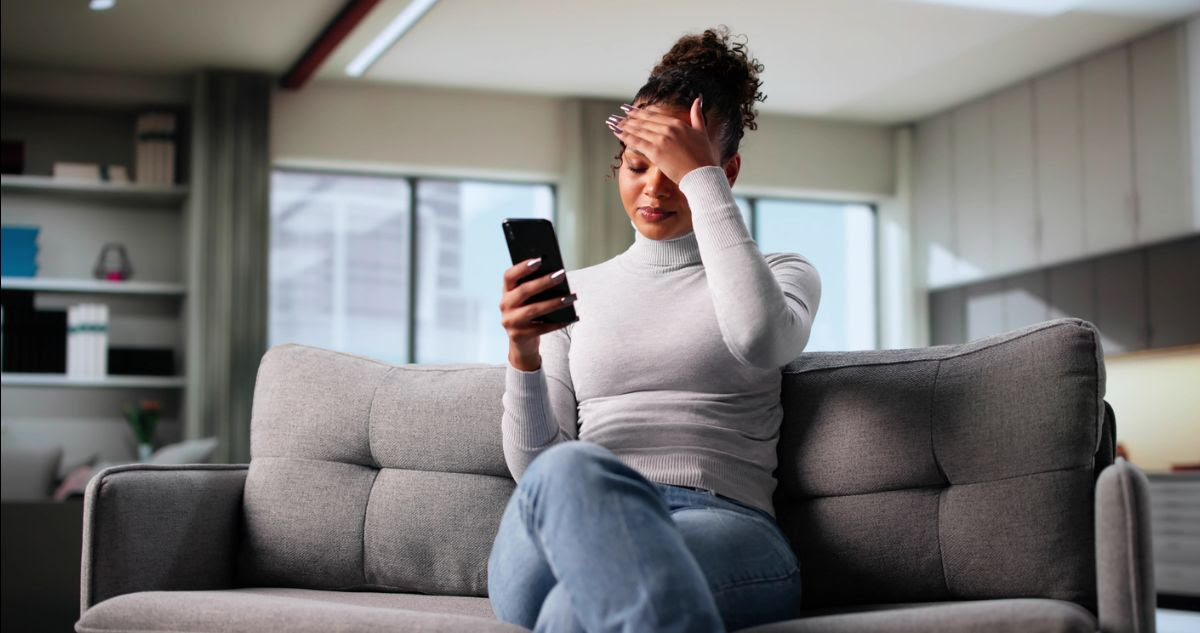 An image of an anxious woman looking at her phone in a living room, symbolizing the rise of stress and anxiety amongst modern Americans 