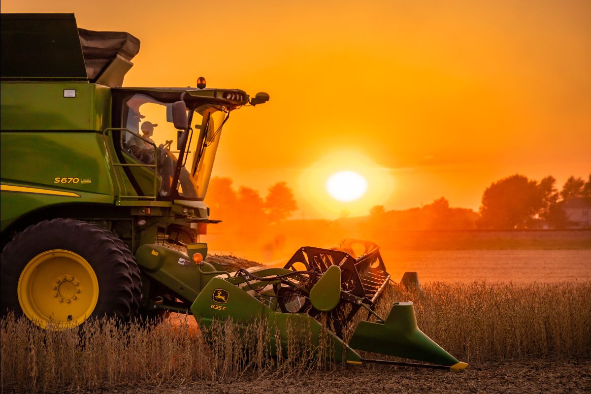 Combine harvester working in a field at sunset, representing real economy production and commodity cycles