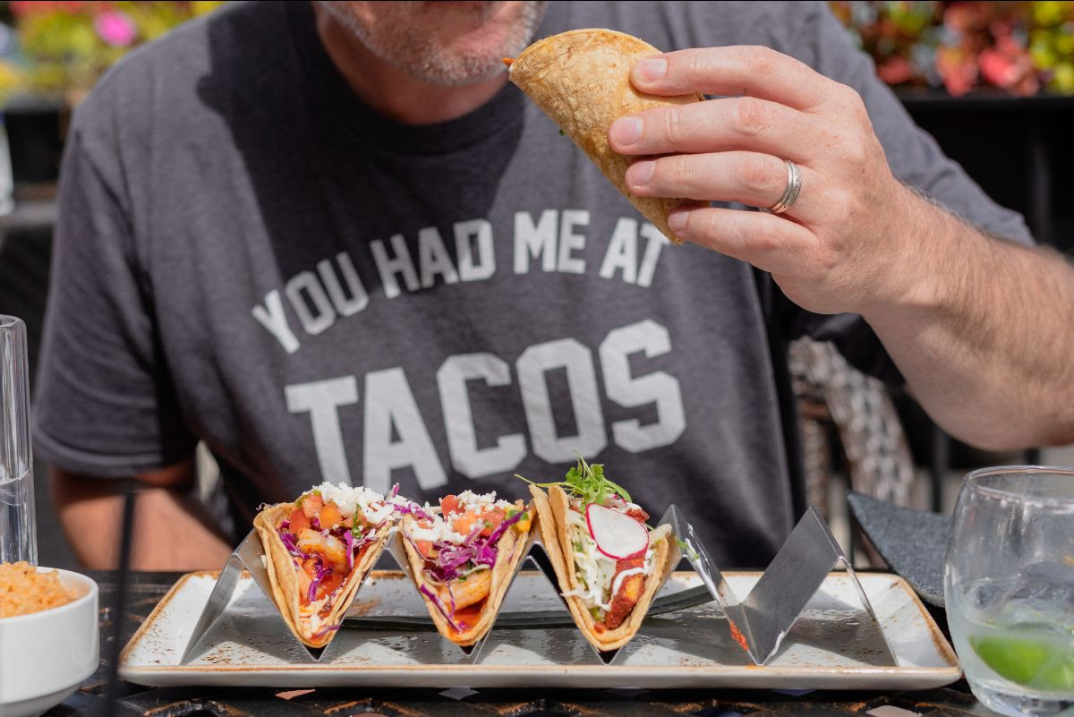 Person eating a taco from a rack of four tacos, symbolizing the potential of Trump to "taco" 